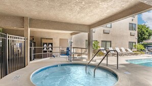 A covered outdoor swimming pool with a hot tub, lounge chairs, and a building in the background. - Best Western Plus Park Place Inn - Mini Suites (Anaheim)