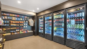 A self-service snack and drink station with refrigerated beverage dispensers and shelves stocked with snacks and packaged foods. - Best Western Plus Park Place Inn - Mini Suites (Anaheim)