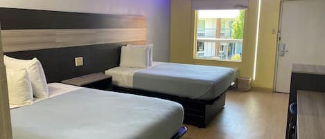 Ein Hotelzimmer mit zwei Betten, einem Schreibtisch und einem Fenster mit Blick auf Gebäude.