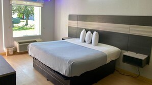 A modern bedroom with a large bed, bedside tables, a built-in shelf, and a window with a view of the outdoors. - Rest and Relax Inn (Pensacola)