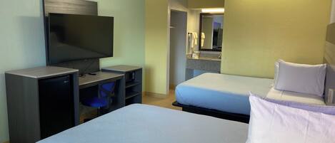 A hotel room with two beds, a desk with a television, and a bathroom visible through an open door.