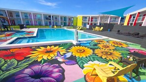 A hotel pool area with a colorful mural, sunflowers, and lounge chairs. - Rest and Relax Inn (Pensacola)