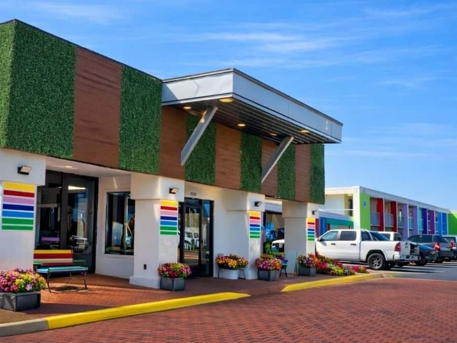A building with a modern design, featuring a green and brown facade, multiple doors, and a brick-paved entrance area.