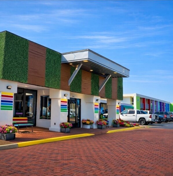A building with a modern design, featuring a green and brown facade, multiple doors, and a brick-paved entrance area. - Rest and Relax Inn (Pensacola)