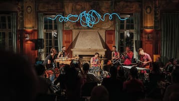 A band performing on a stage with a large audience in a room with ornate walls and a fireplace.