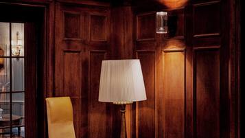 Una habitación con paneles de madera, un sillón amarillo, un sofá de cuero negro, una lámpara y una mesa con un libro.