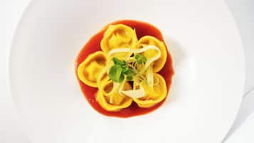 A white plate with ravioli in a red sauce, garnished with microgreens and shaved cheese.