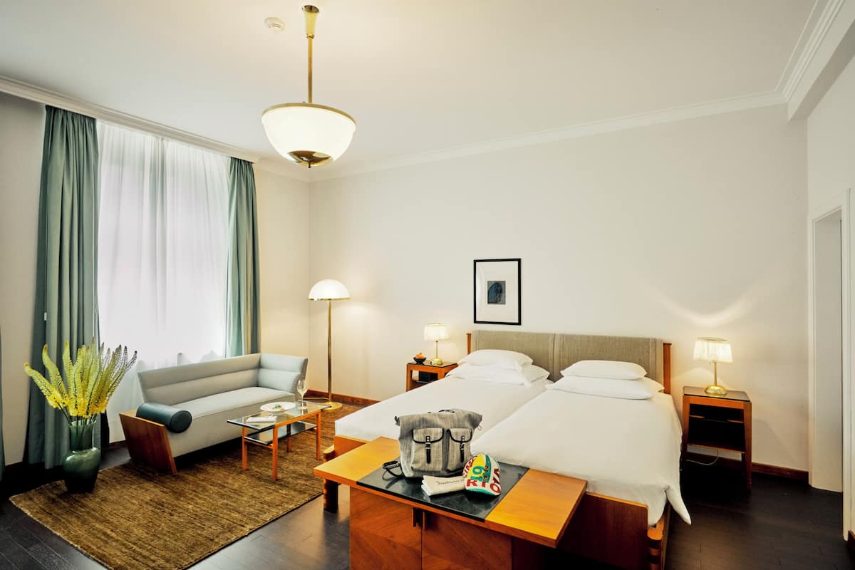 Ein Hotelzimmer mit Bett, einer Couch, einem Schreibtisch, einer Lampe, einem Bild an der Wand und einer Pflanze.