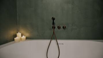 Een bad met douchekop, drie brandende kaarsen en een groene wand.