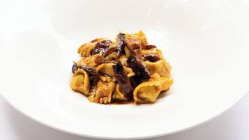 A white bowl of pasta with mushrooms and sauce on a white surface.