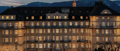 Un hotel grande de varios pisos con una entrada destacada y un paisaje montañoso de fondo.