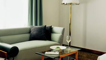 A modern hotel room with a green sofa, a glass coffee table, a lamp, and a view of the outdoors.