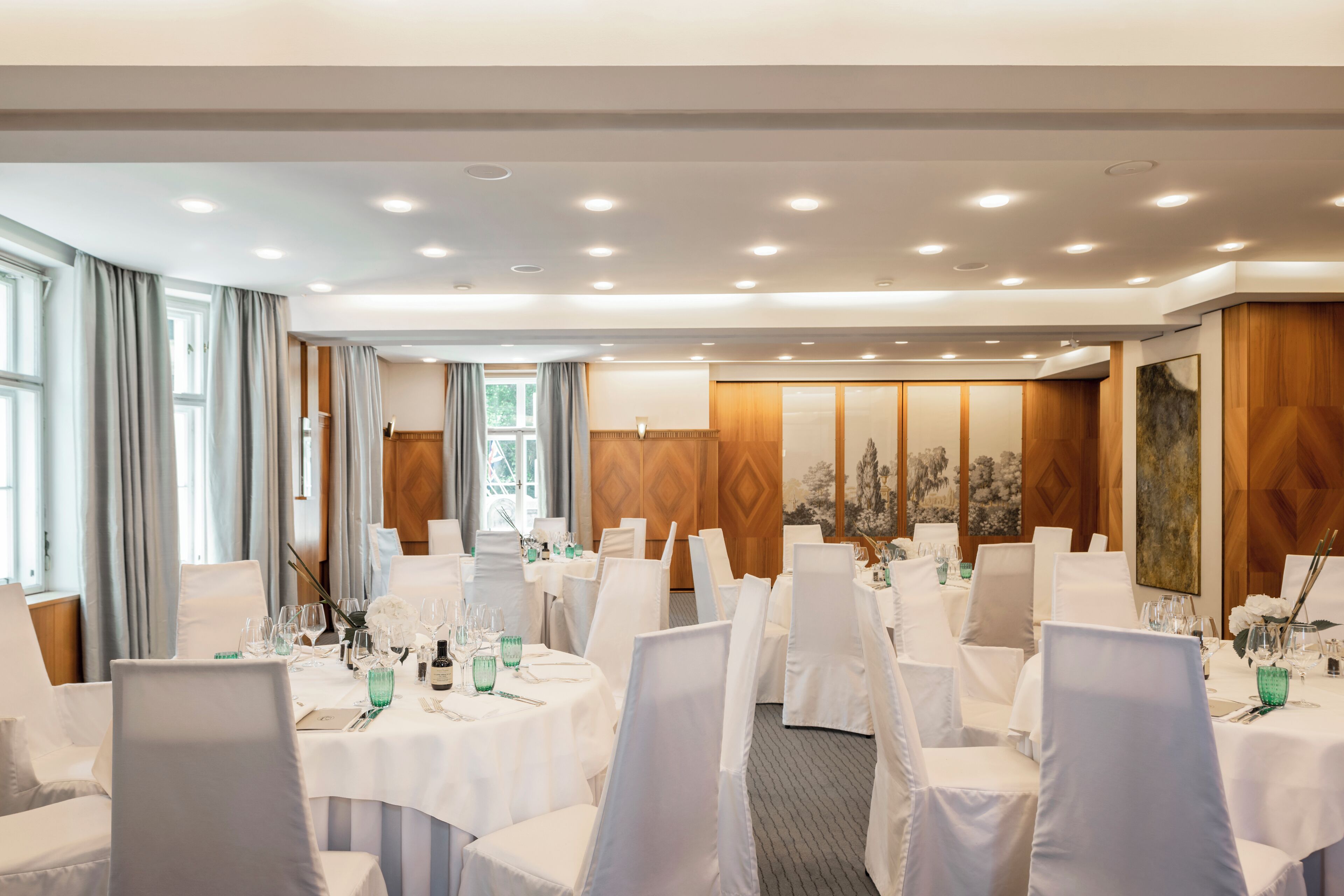 A banquet hall with round tables, white chairs, and a wooden panel wall.