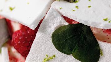 Un dessert composé de mousse blanche, de framboises et de feuilles vertes.