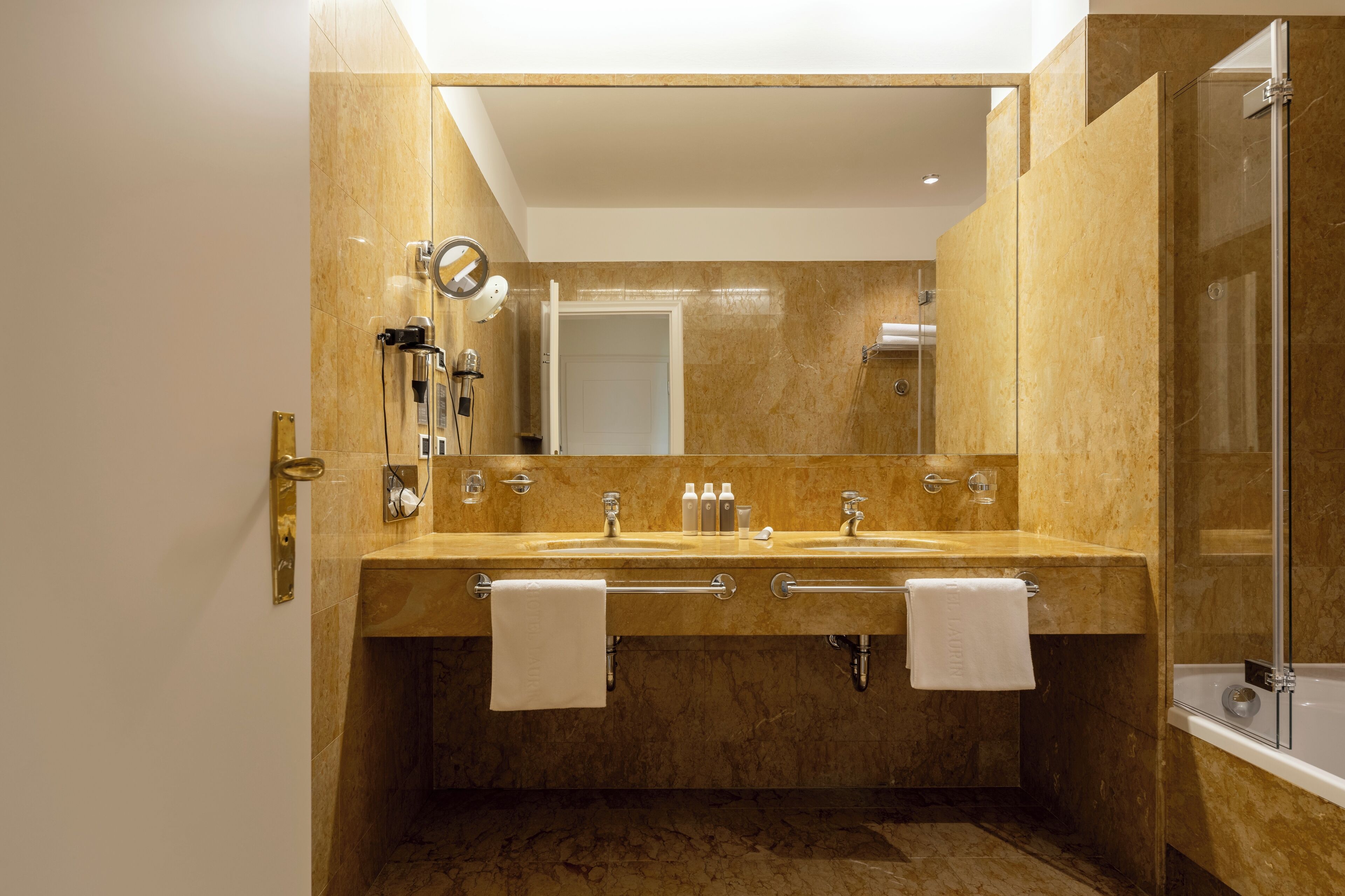 A modern bathroom with a large mirror, dual sinks, and a glass-enclosed shower.