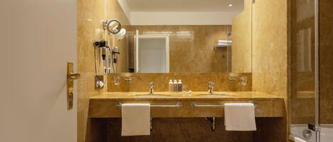 A modern bathroom with a large mirror, dual sinks, and a glass-enclosed shower.