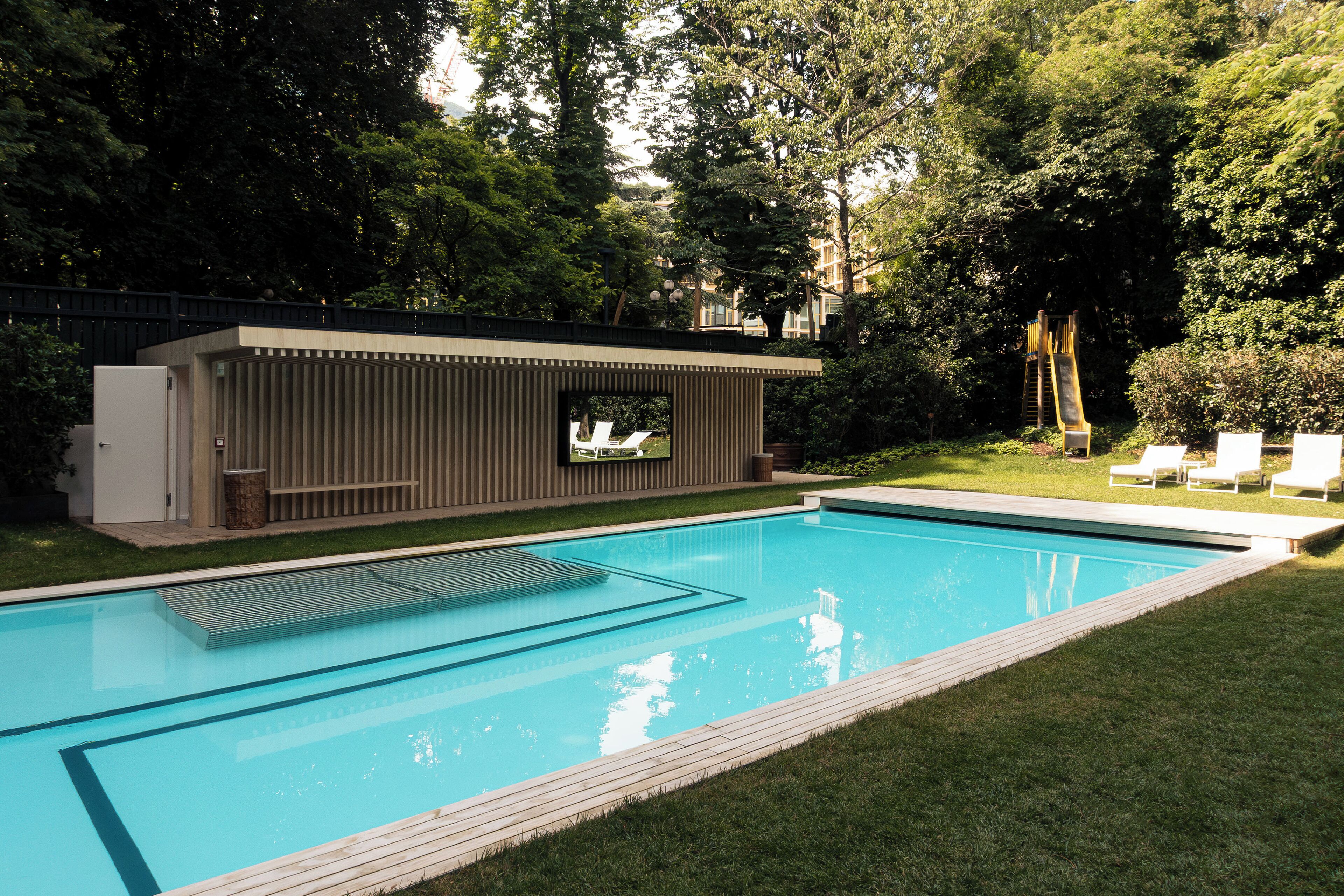 Una piscina con un deck moderno, rodeada de vegetación exuberante y un pequeño espacio de estar al aire libre.