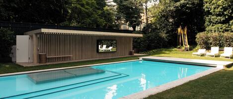 Una piscina con un deck moderno, rodeada de vegetación exuberante y un pequeño espacio de estar al aire libre.