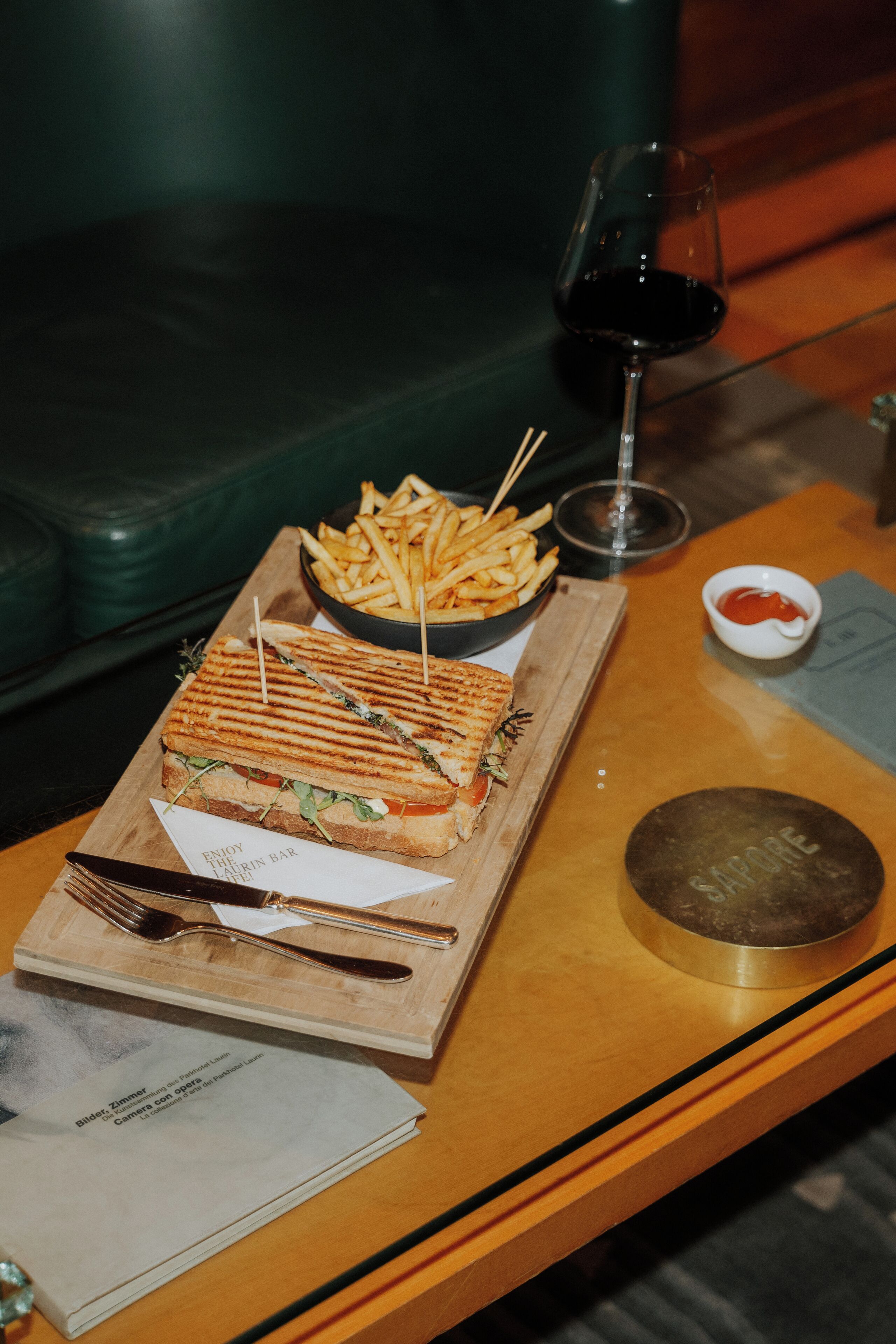 Una bandeja con un sándwich a la plancha, papas fritas y un tazón pequeño de kétchup sobre una mesa de madera.