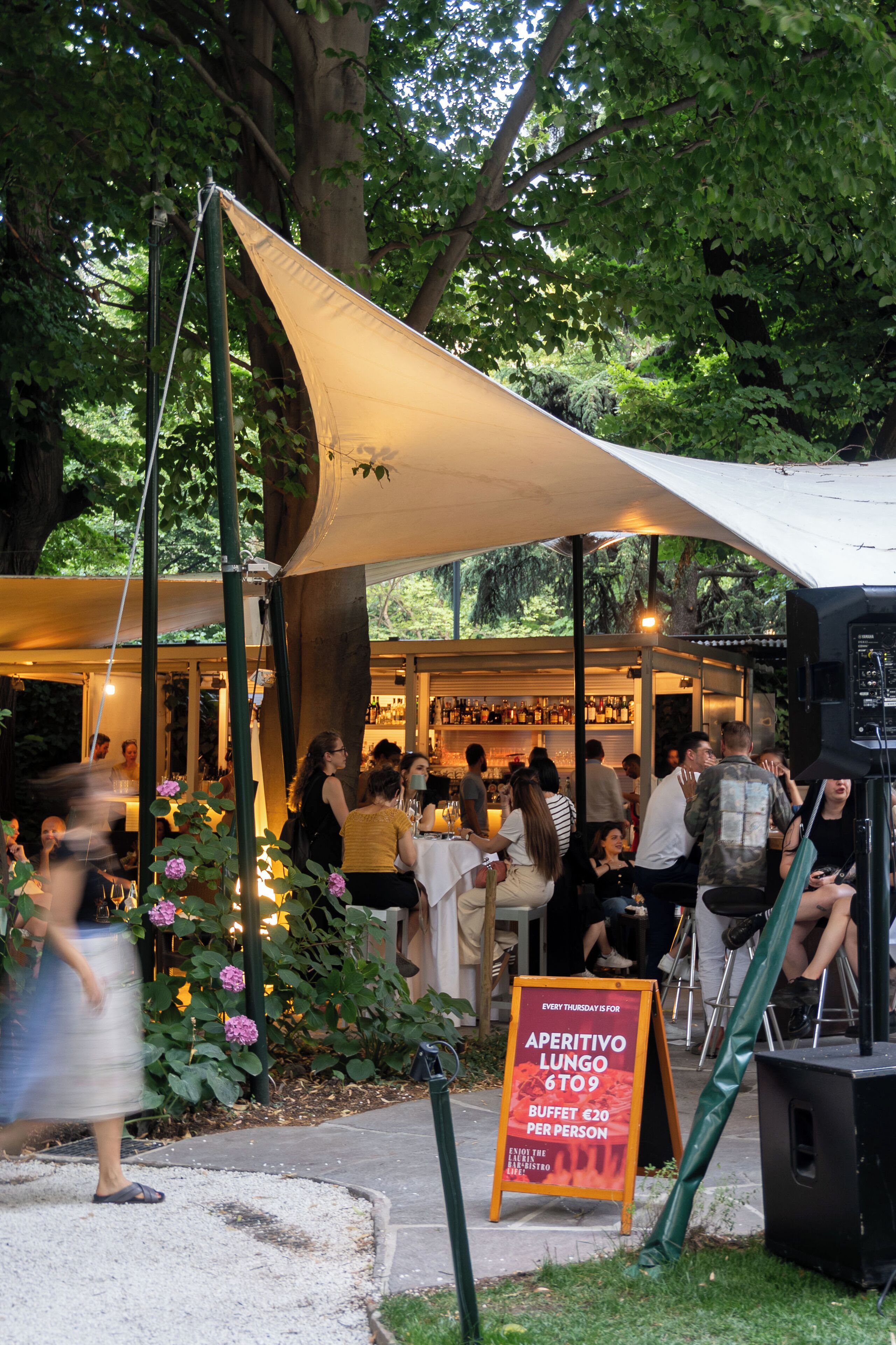 Een terras met een overkapping, omringd door groen en een bar op de achtergrond.