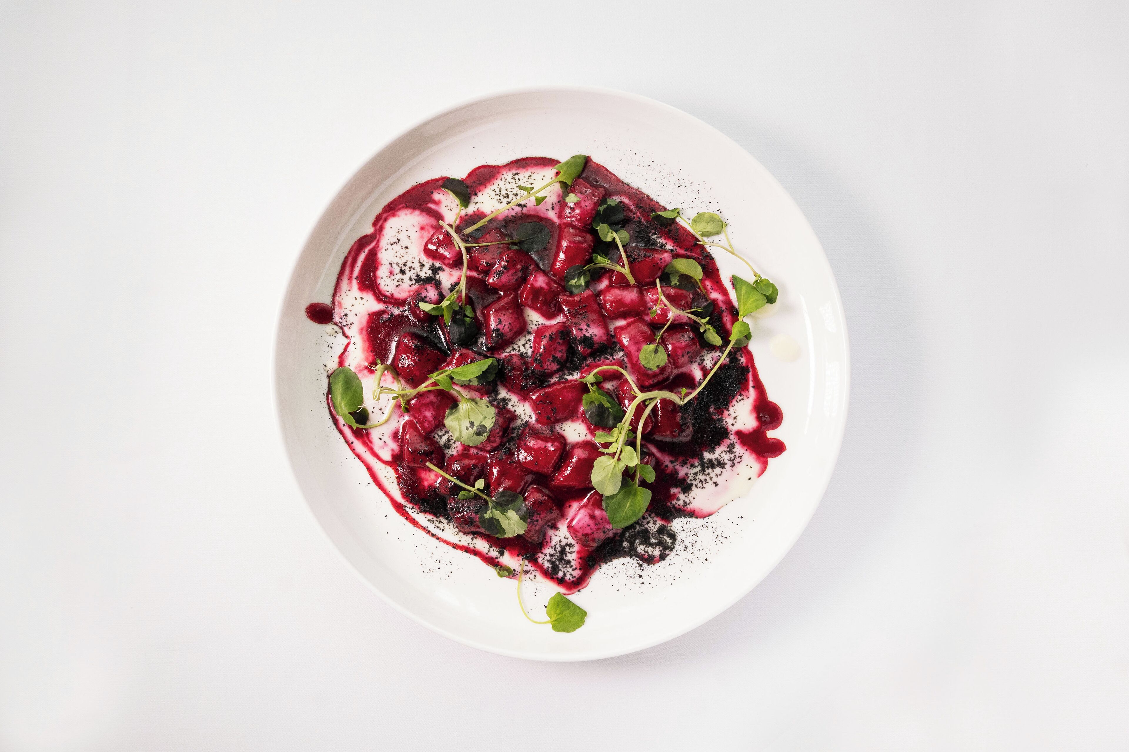 A white plate with a beetroot salad, blackberries, and microgreens.