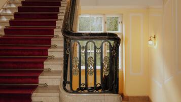 Un magnifique escalier, avec un tapis rouge, une rampe en métal ouvragée et des appliques murales.
