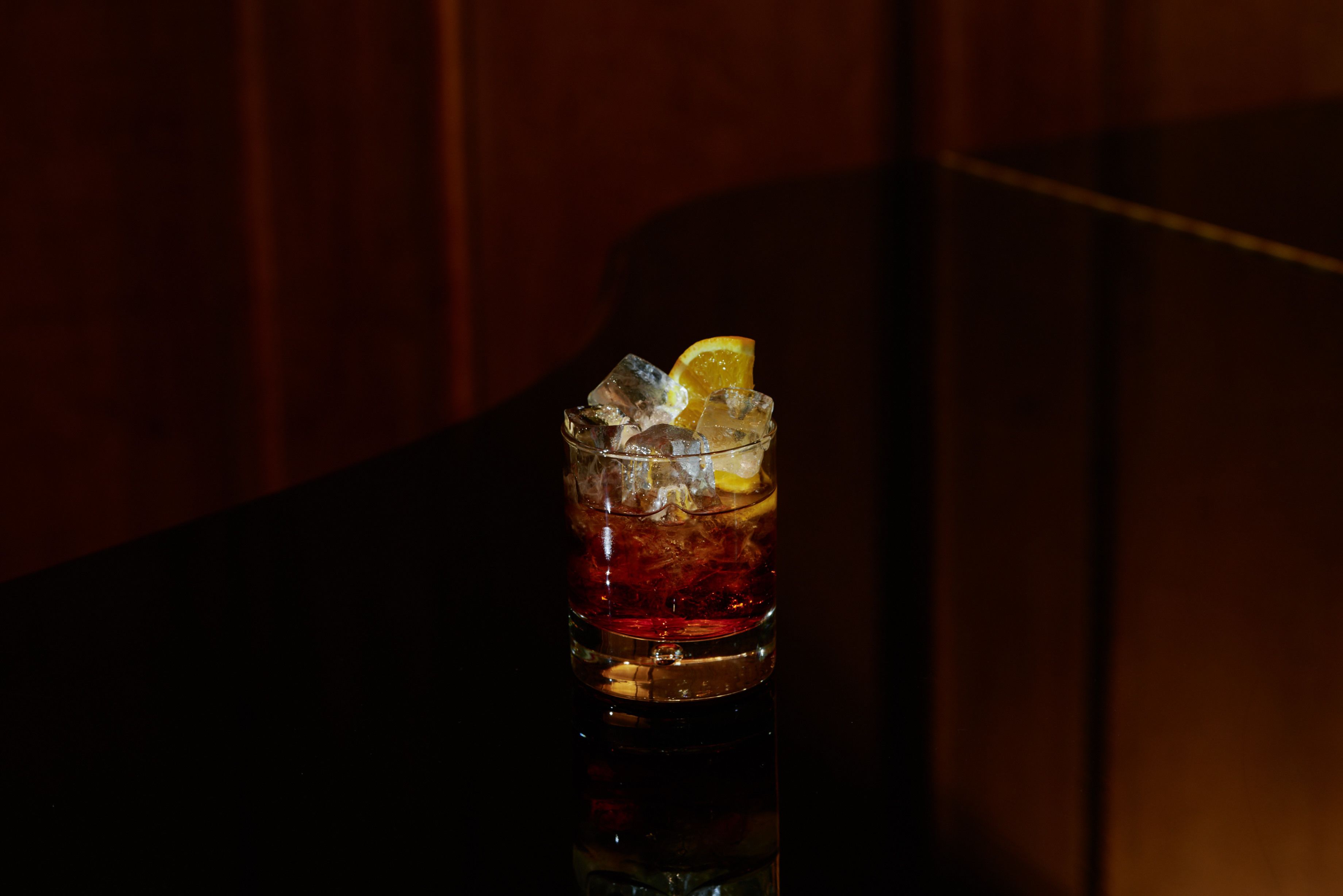 A glass of iced beverage with ice cubes and a slice of lemon.
