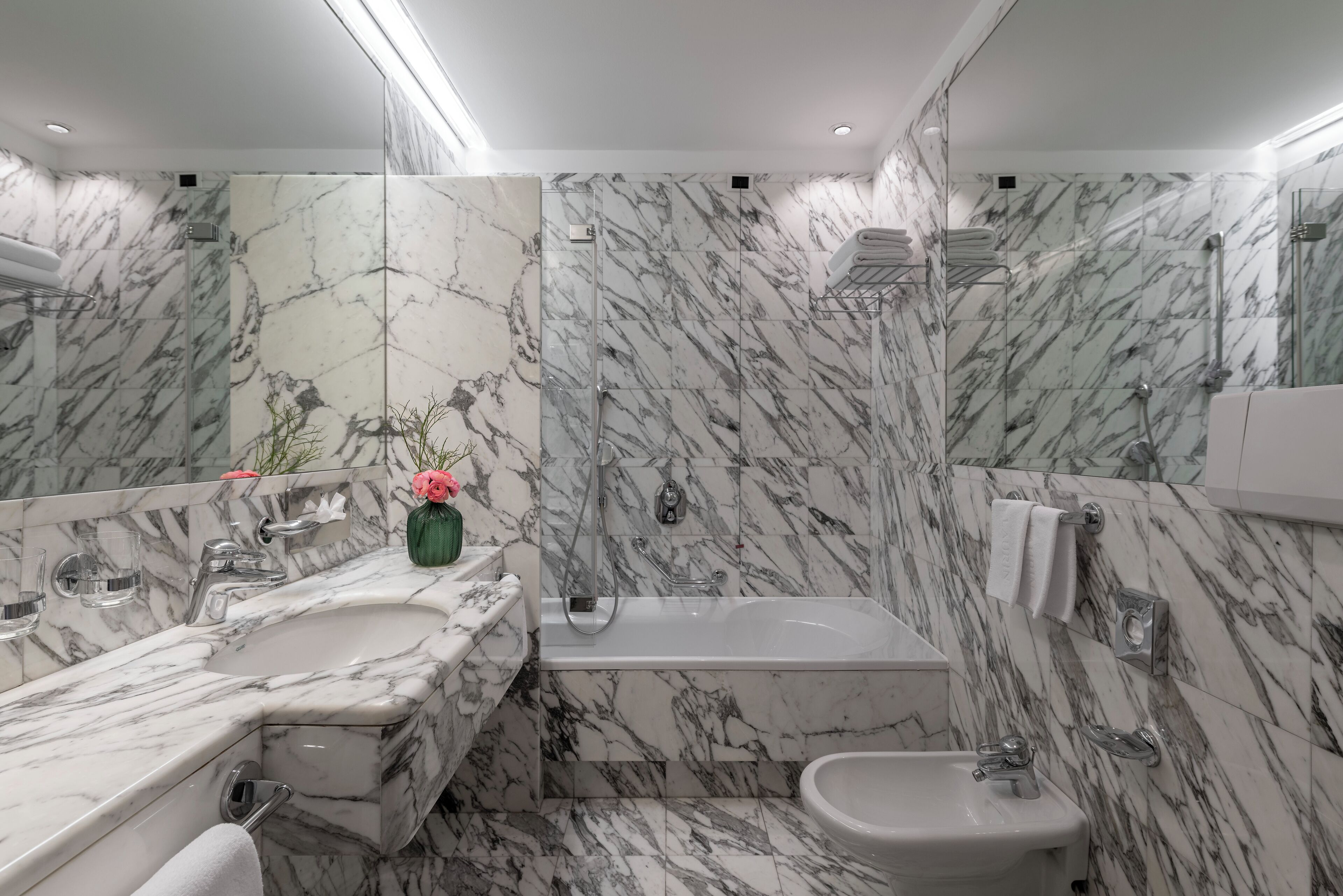 A modern bathroom with marble walls, a large bathtub, a sink, and a bidet.
