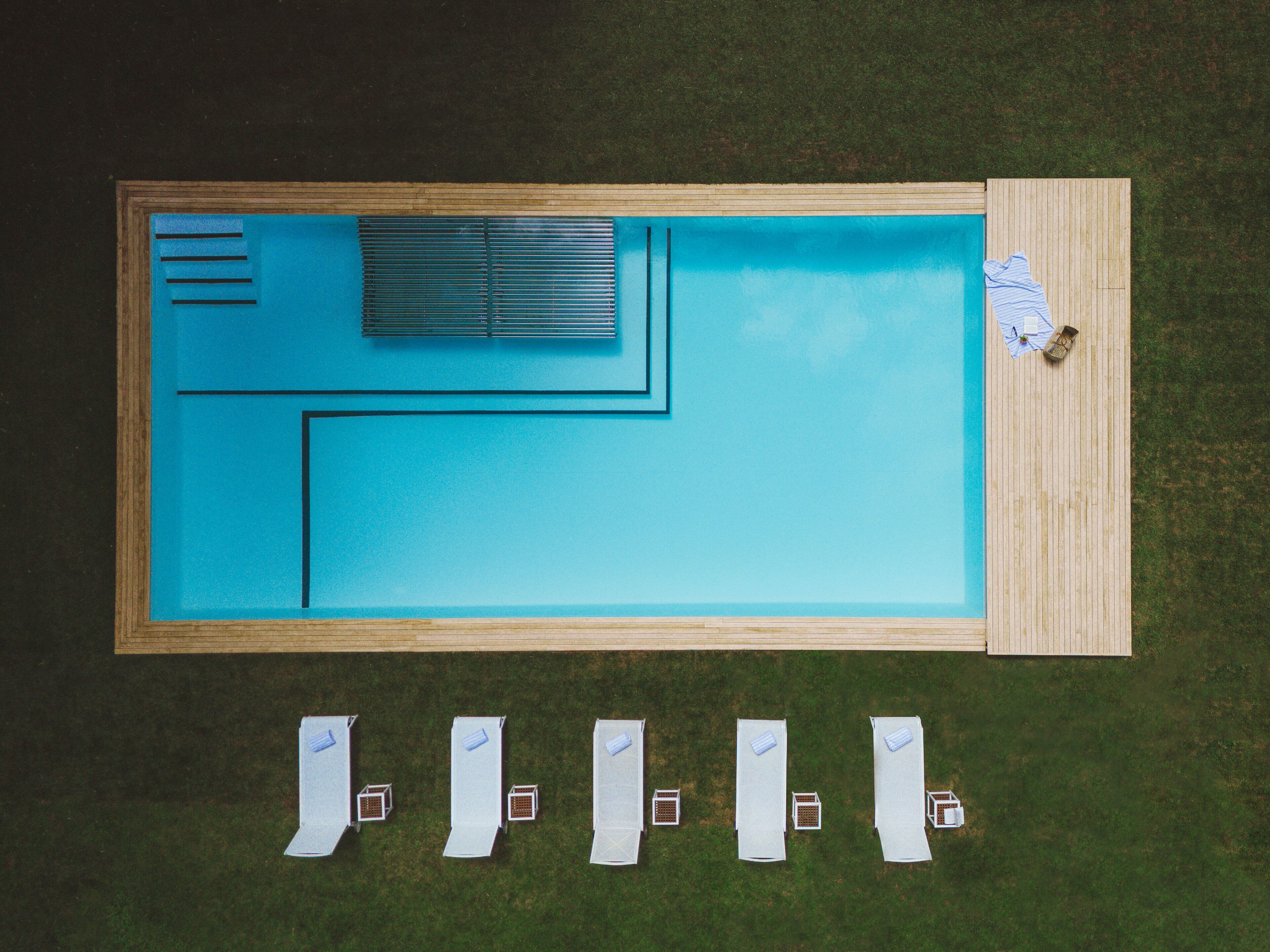 Une piscine rectangulaire dotée d’une terrasse en bois et d’un espace ombragé avec des parasols.