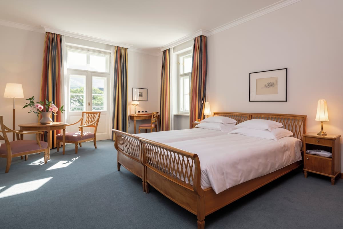 Ein Hotelzimmer mit einem großen Bett, einem Schreibtisch mit Stuhl, einem kleinen Tisch mit Vase und einem Nachttisch mit Lampe.