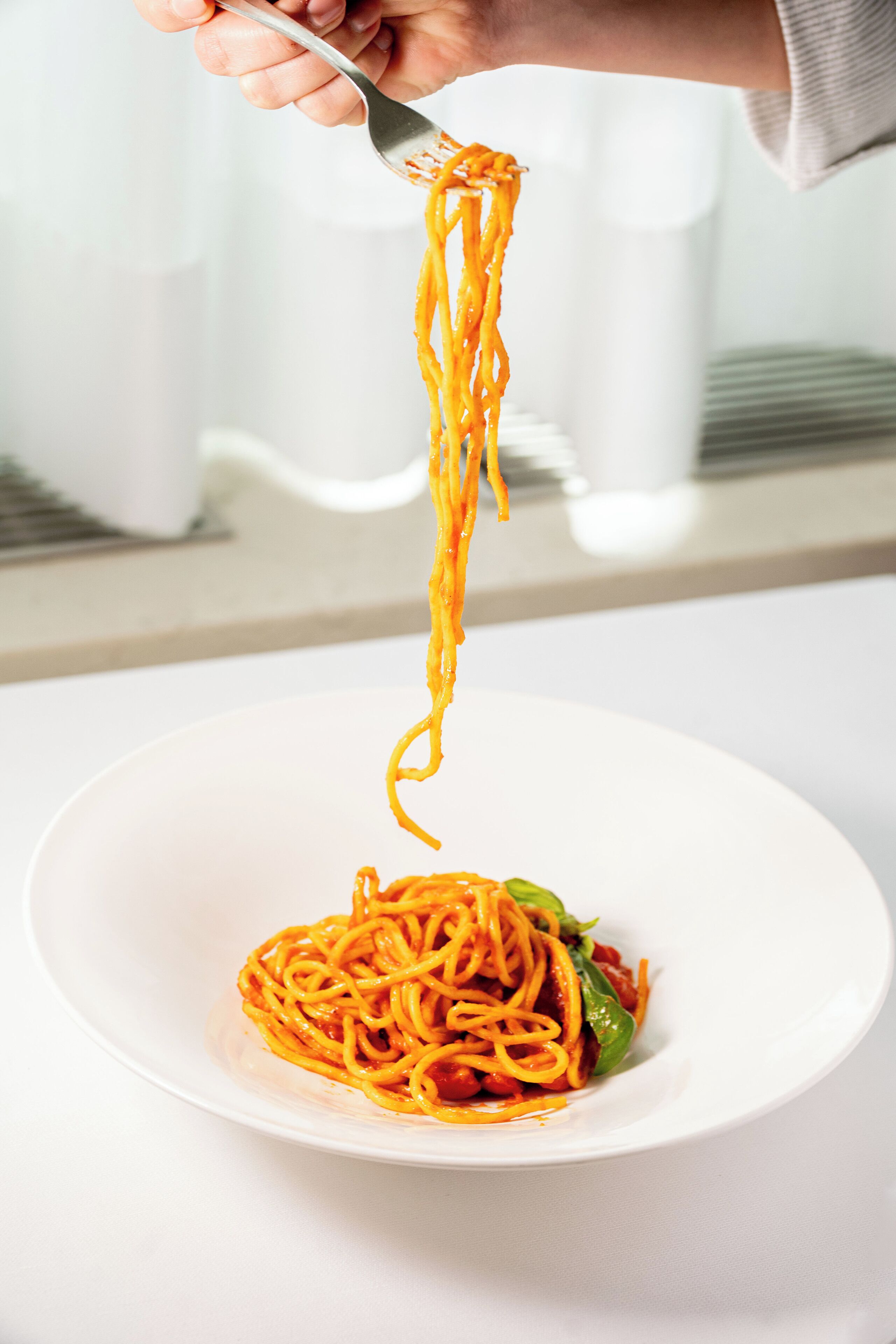 A person holding a fork with spaghetti over a white plate.