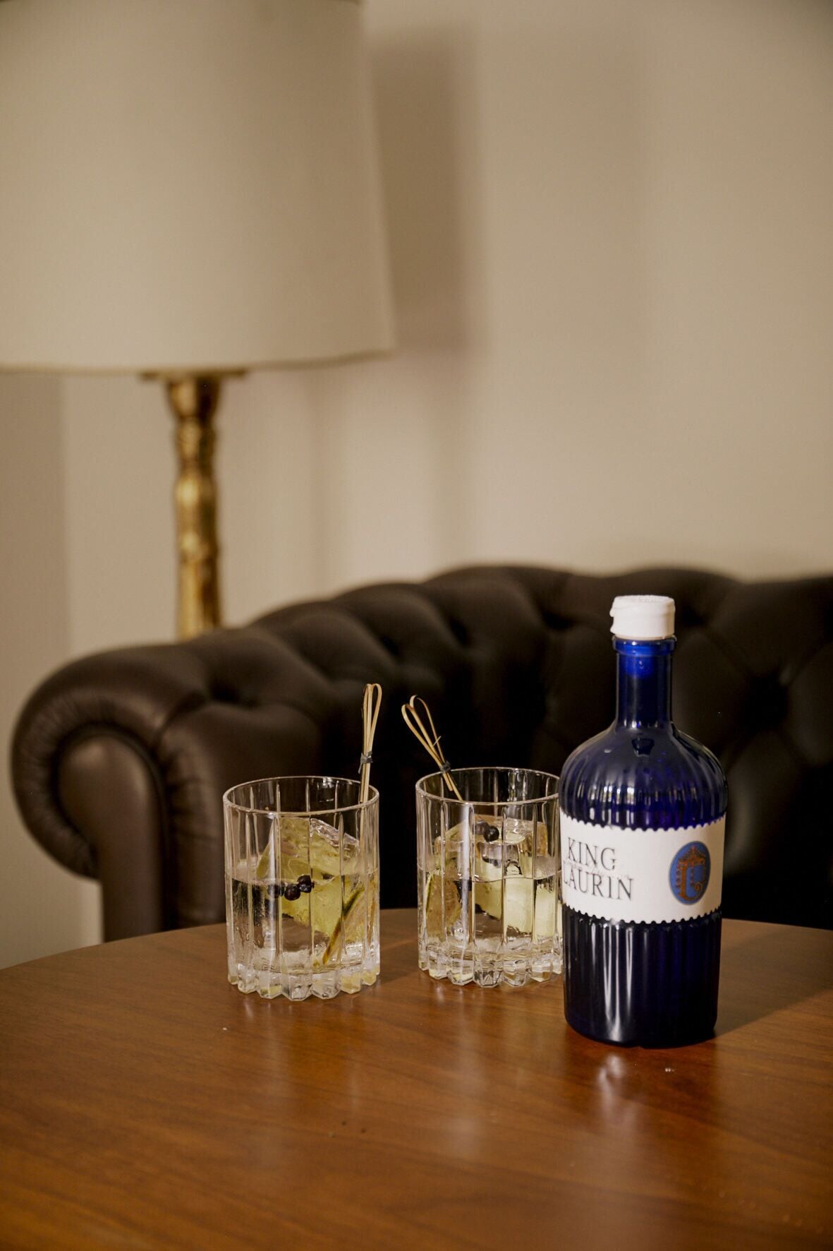 A bottle of King Laurin on a table with two glasses containing ice and a drink.