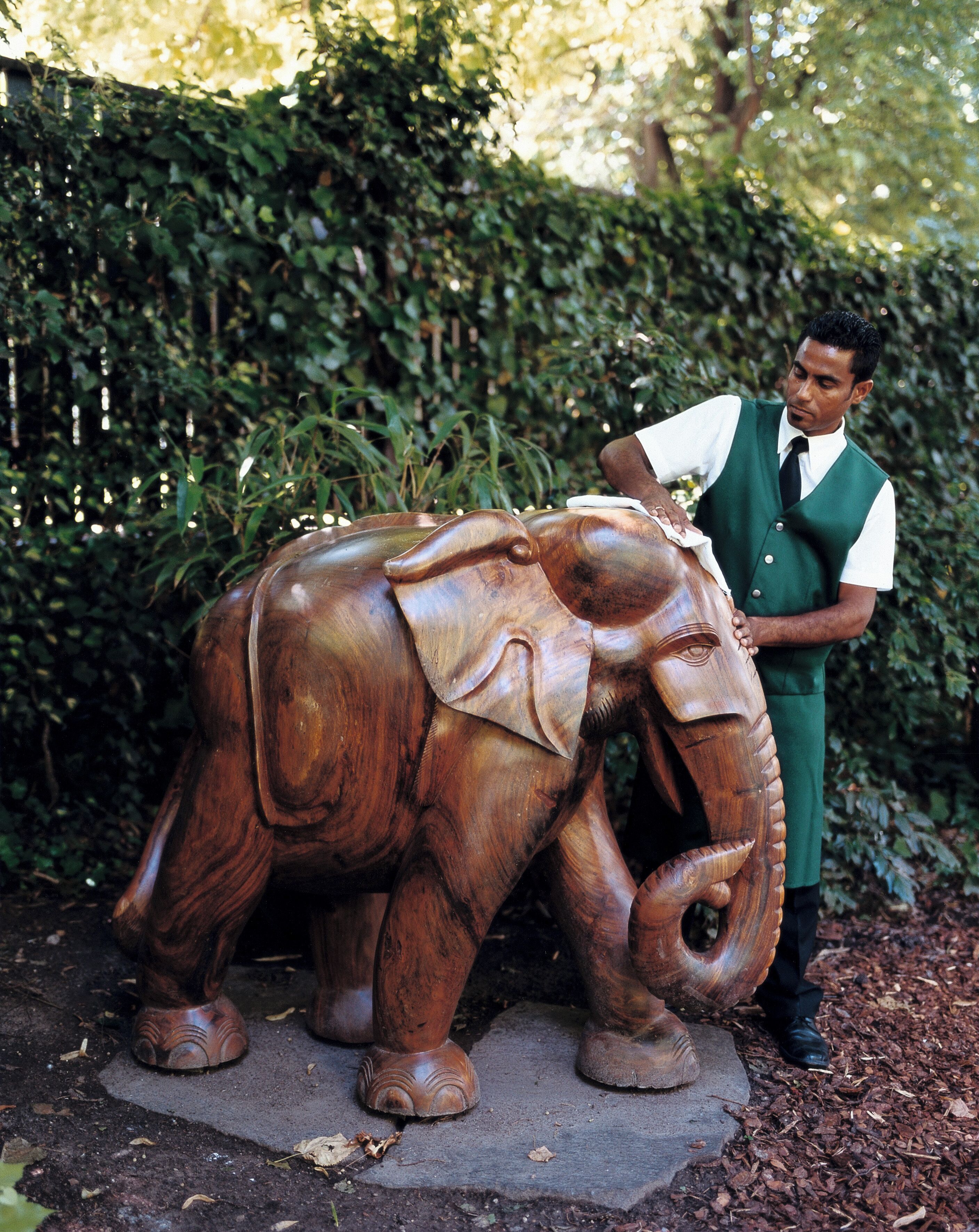 Un uomo in piedi accanto a una scultura di elefante in legno in un giardino.