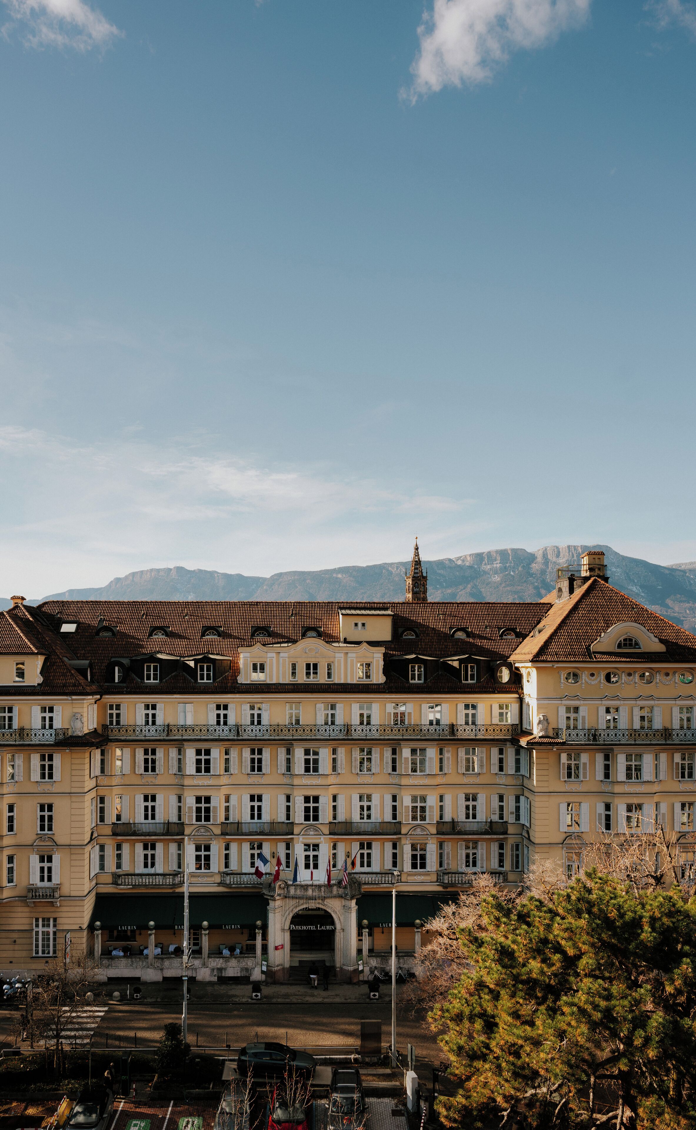 Ein mehrgeschossiges Gebäude mit einem zentralen Eingang, Balkonen und einer Bergkulisse.