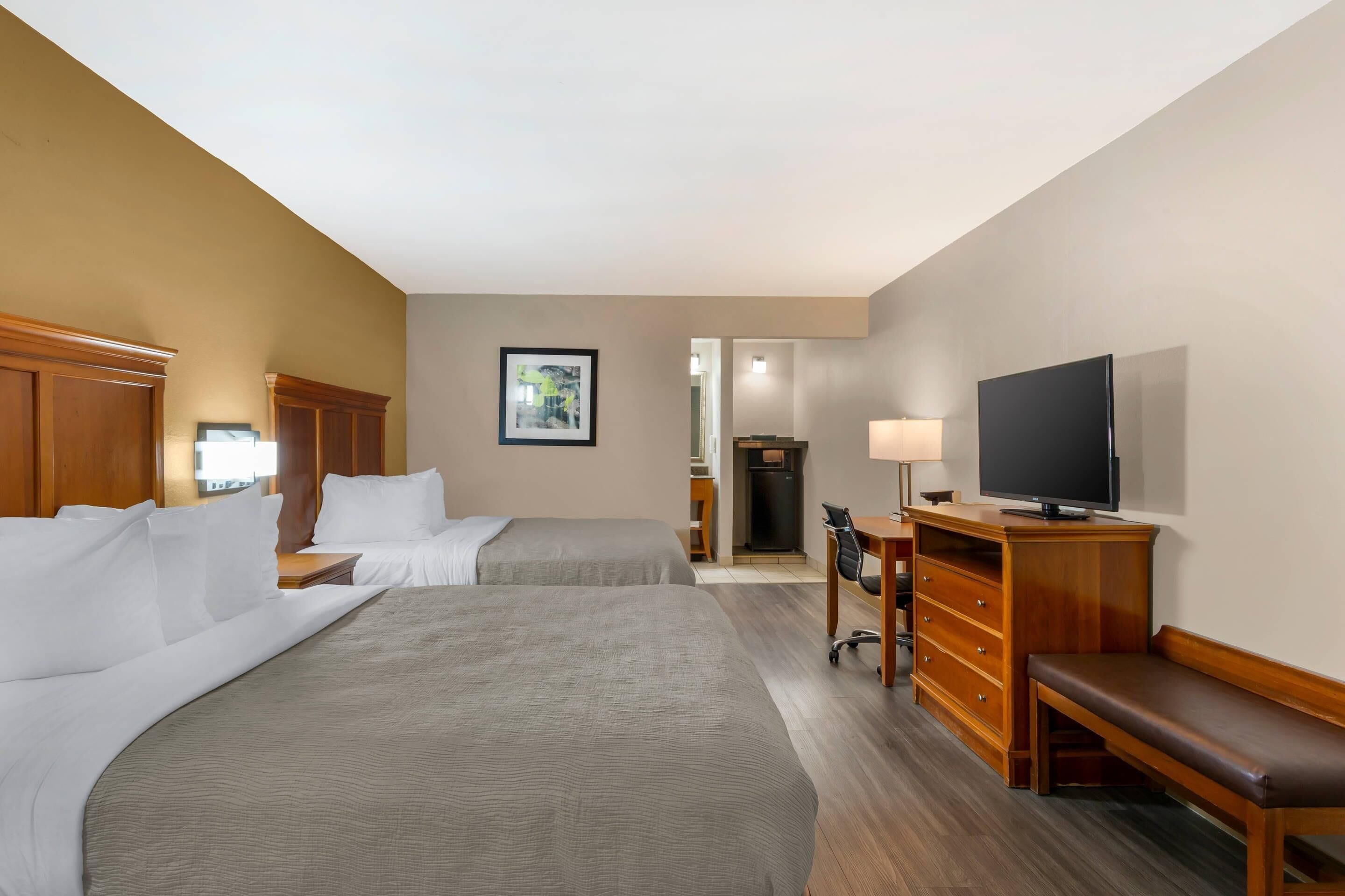 A hotel room with two beds, a TV, a desk, and a chair.