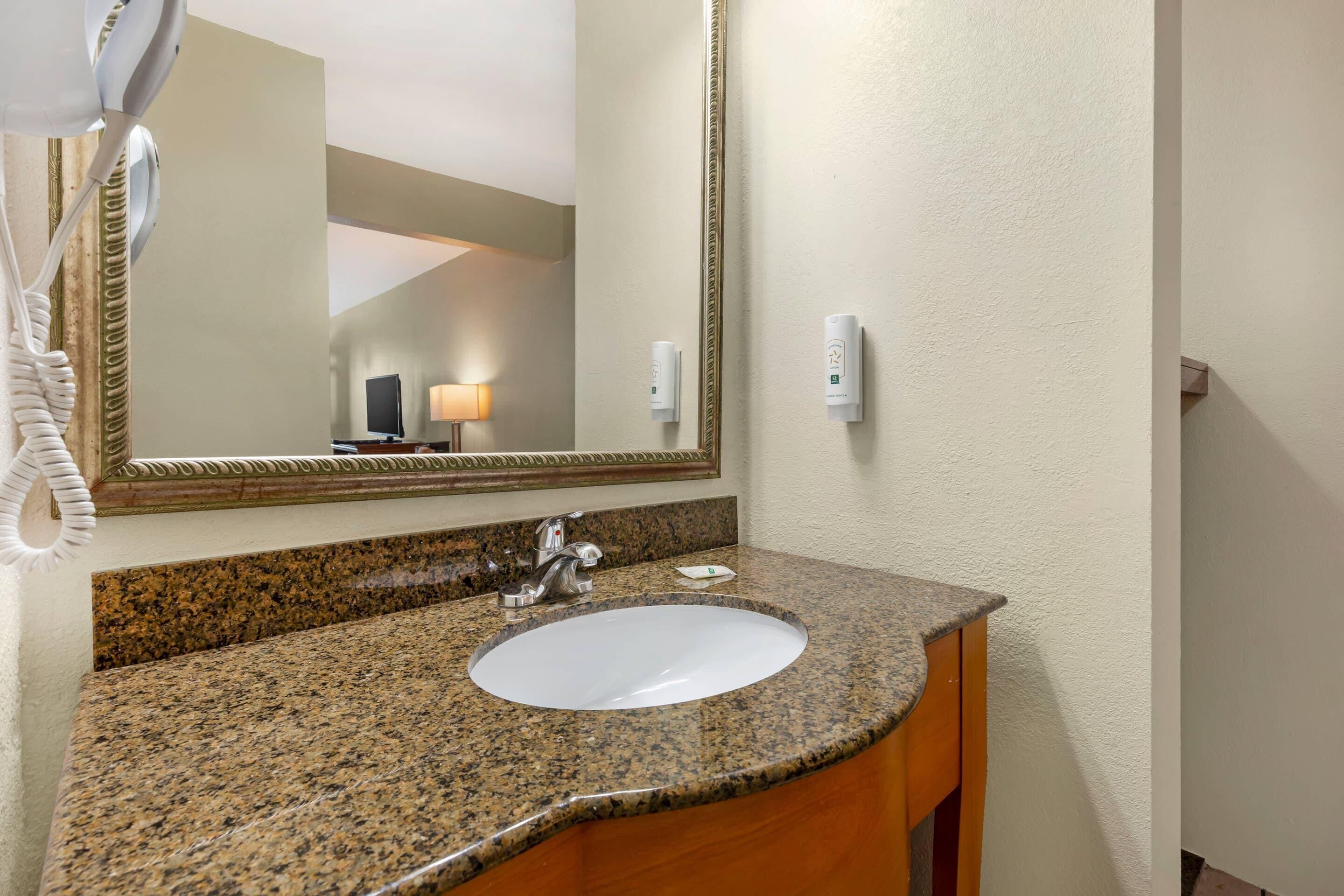 A bathroom with a granite countertop, a white sink, a mirror, and a towel rack.