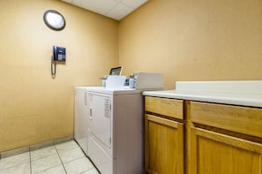 Convenient laundry facilities with a wall-mounted phone, clock, and stacked machines.
