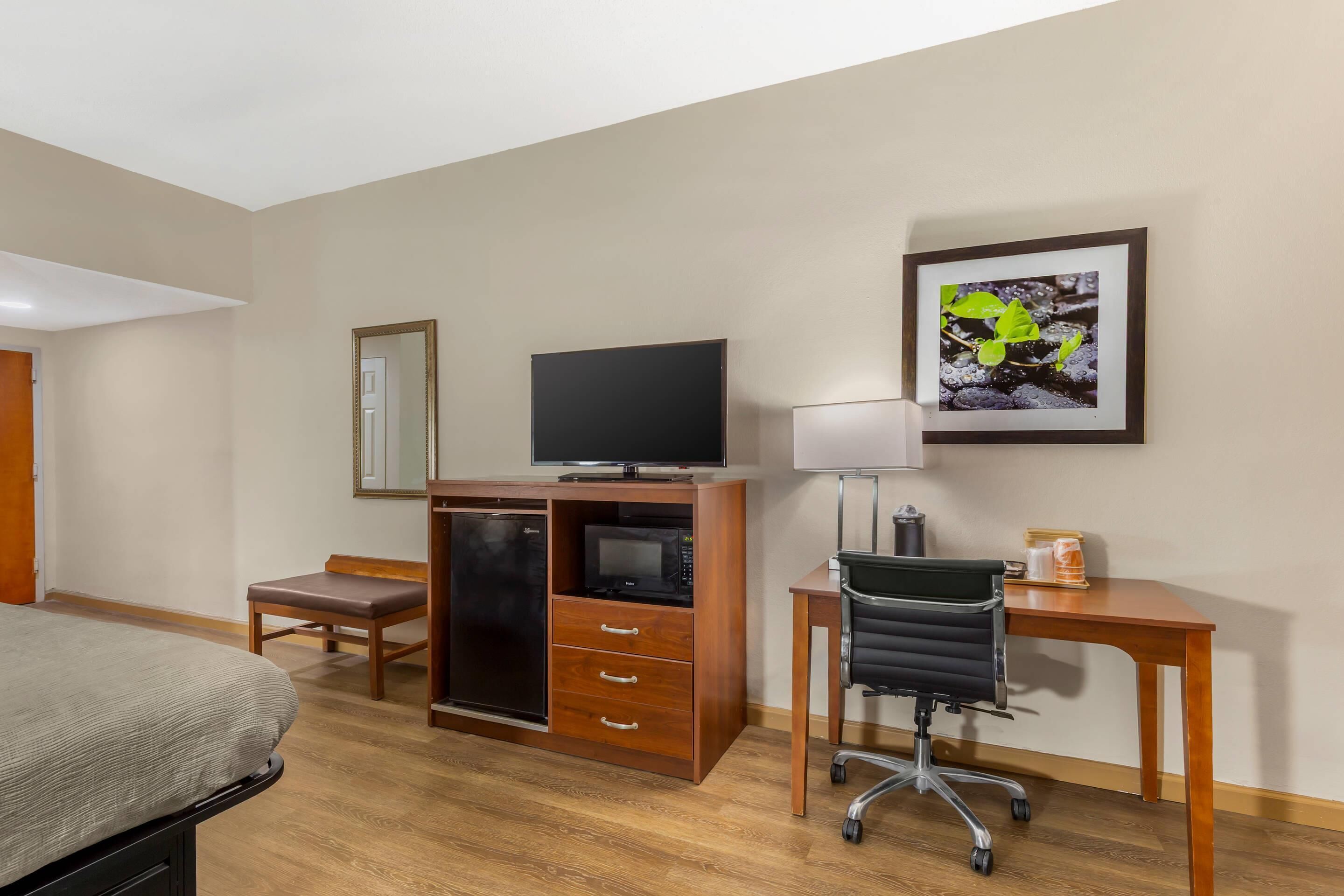 Una camera d'albergo con un letto, una scrivania con una sedia, una televisione, un frigorifero e un forno a microonde.