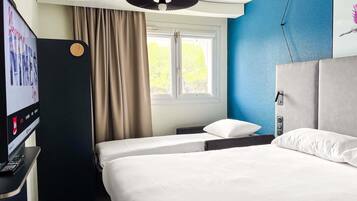 A hotel room with a bed, a TV, a window with curtains, and a blue wall.