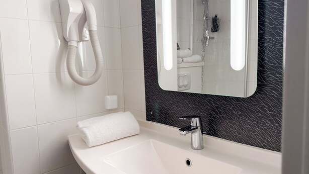 A bathroom with a white sink, a mirror, and a hairdryer mounted on the wall. - ibis Nimes Ouest (Nîmes)