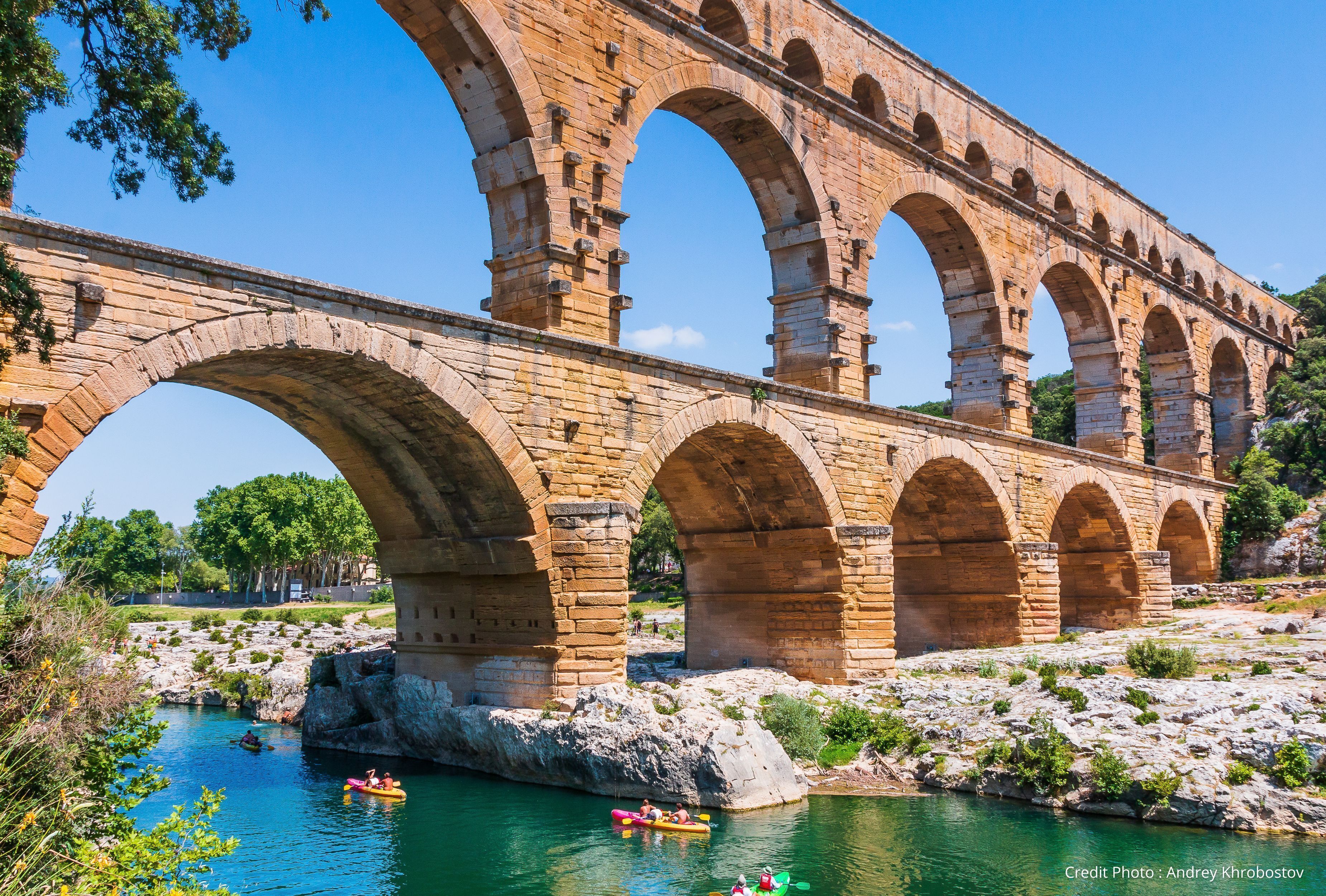 A stone aqueduct bridge over a river with people kayaking.