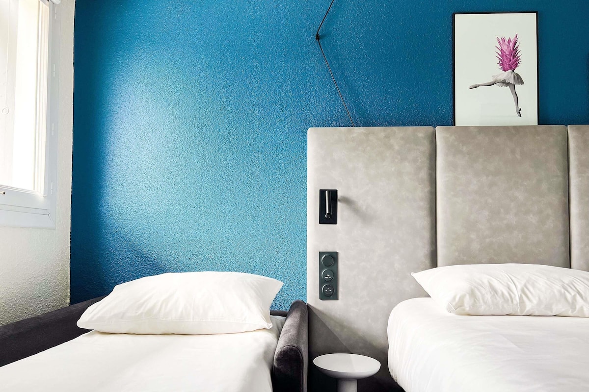 A hotel room with two beds, a small round table, and a painting on the wall.