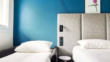 A hotel room with two beds, a small round table, and a painting on the wall.