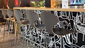 A bar area with black and white patterned wallpaper, modern bar stools, and hanging pendant lights. - ibis Nimes Ouest (Nîmes)