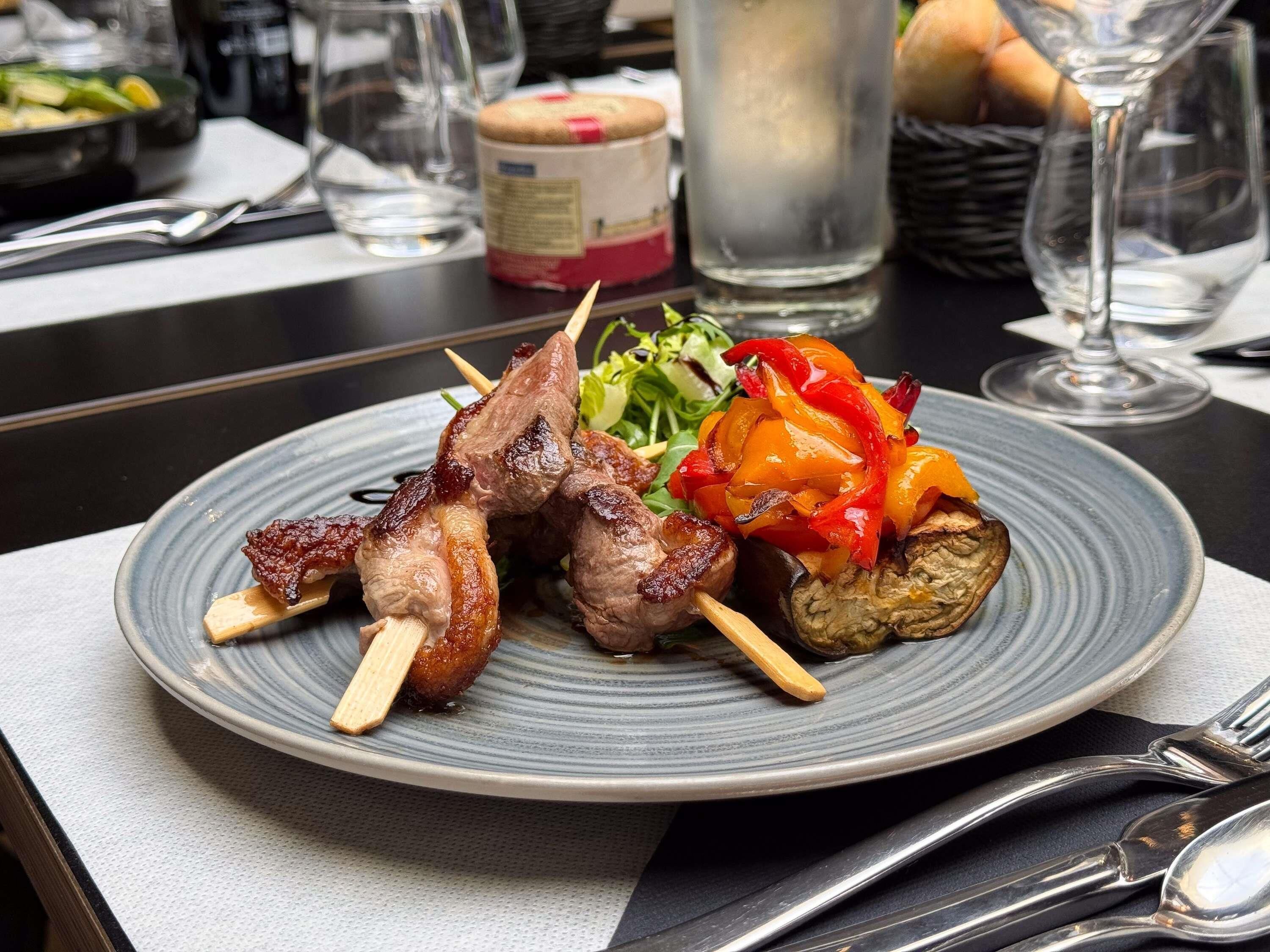 Un plato de comida con brochetas, un vaso de agua y una botella de salsa sobre una mesa.
