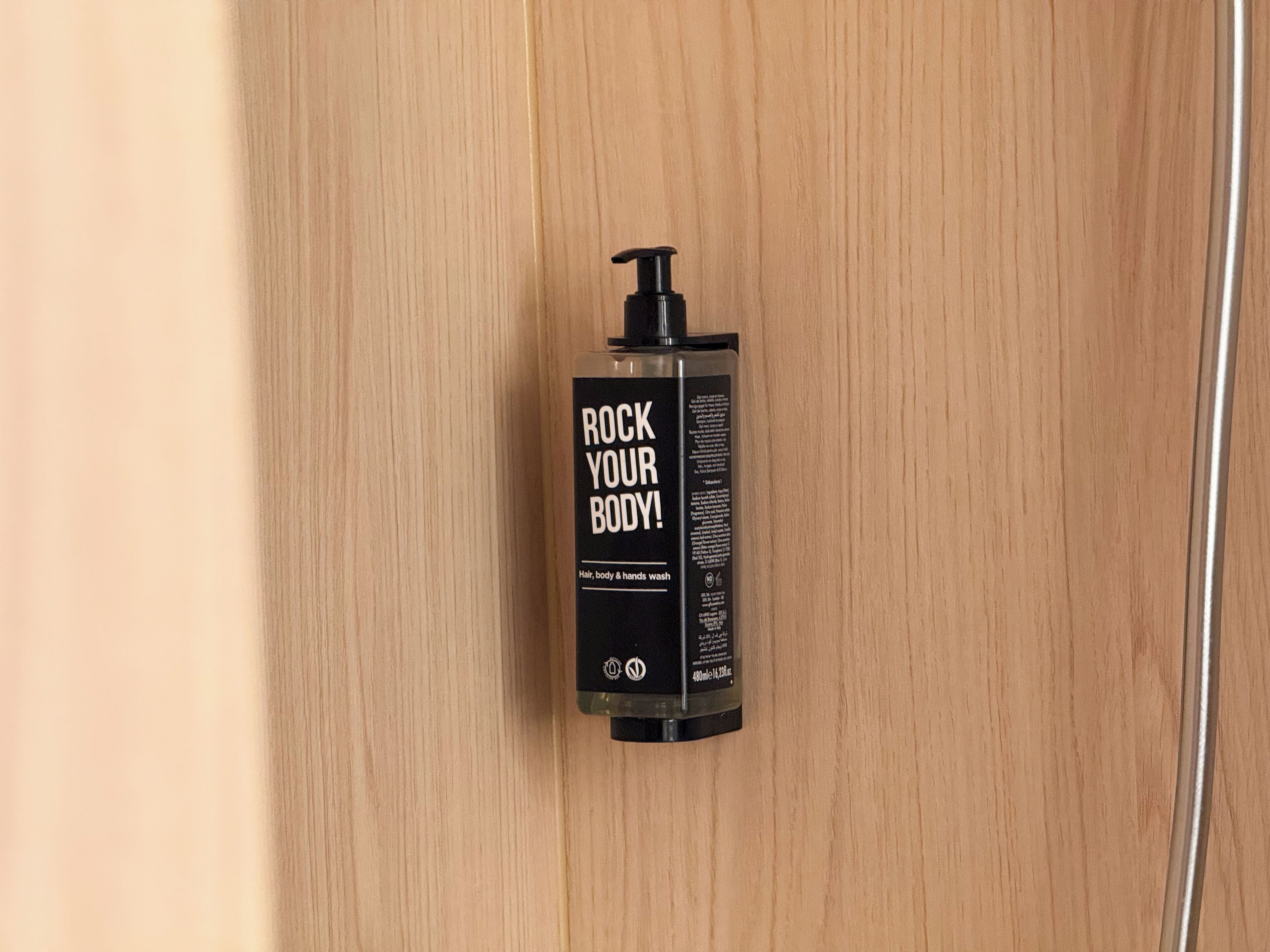 A black bottle with a pump dispenser labeled 'ROCK YOUR BODY!' on a wooden surface.
