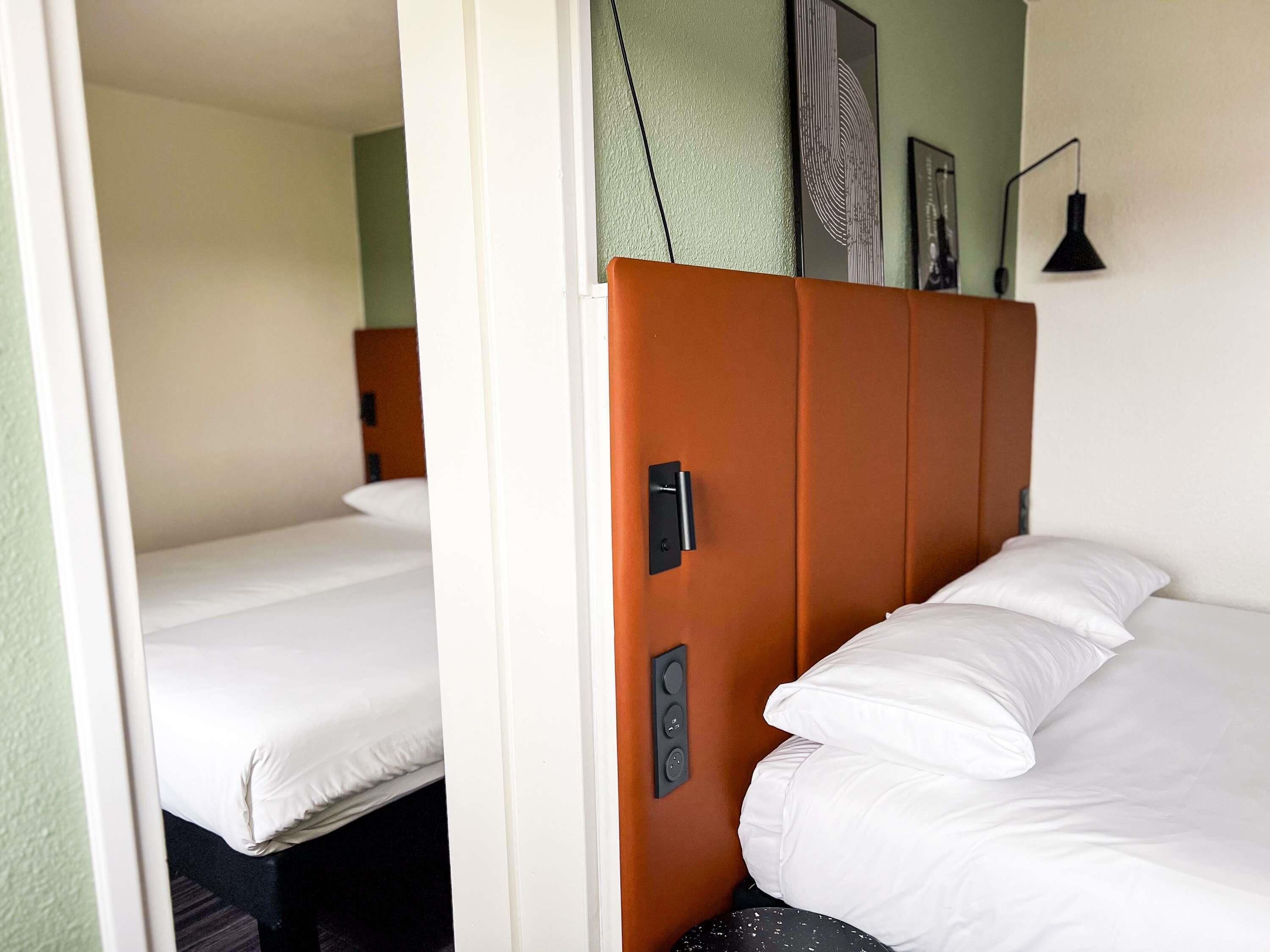 Habitación de hotel con cama, puerta con manija, lámpara de pared e imagen enmarco.