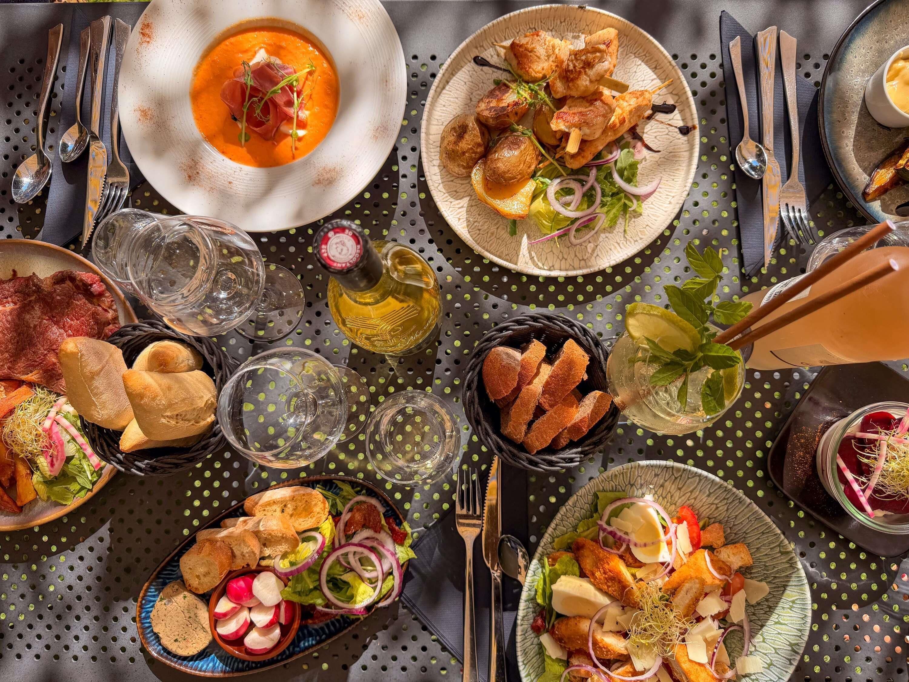 Una mesa servida con varios platos, incluyendo un tazón de sopa, carne ensartada y una ensalada.