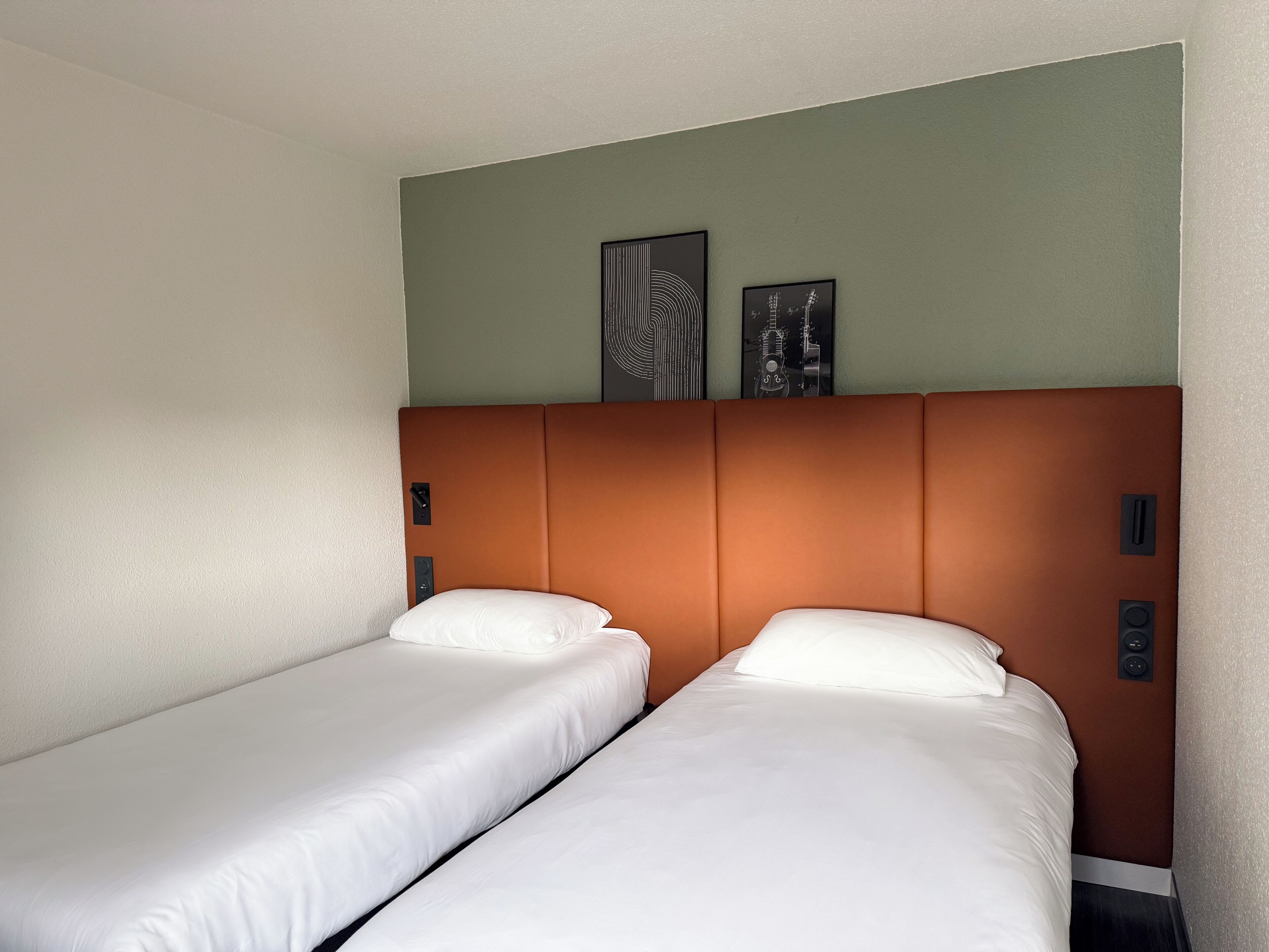 A hotel room with two single beds, a brown headboard, and two wall-mounted artworks.