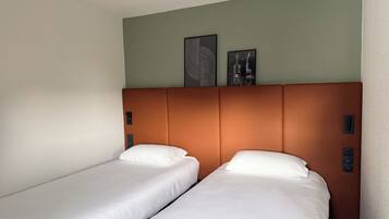 A hotel room with two single beds, a brown headboard, and two wall-mounted artworks.